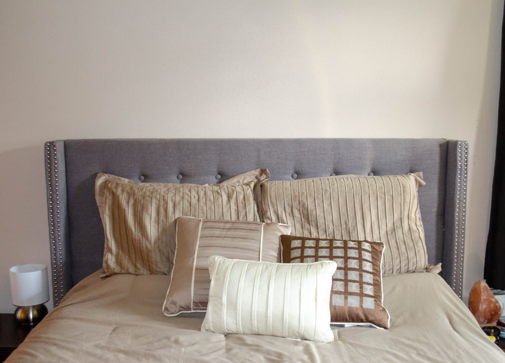 made bed with decorative pillows, gray headboard and taupe comforter