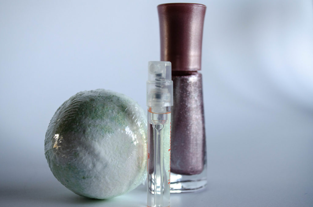a green and white bath bomb, a perfume sampler and a pin kmetallic nail polish